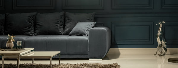 Dark modern sofa with plush cushions in a minimalist living room with a panelled wall and decorative sculpture