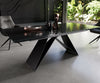 Modern black dining table with textured glass top and wave-like metal base in a bright room.