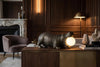 Hippopotamus-shaped lamp on a wooden table in a stylish room with a fireplace and armchair.